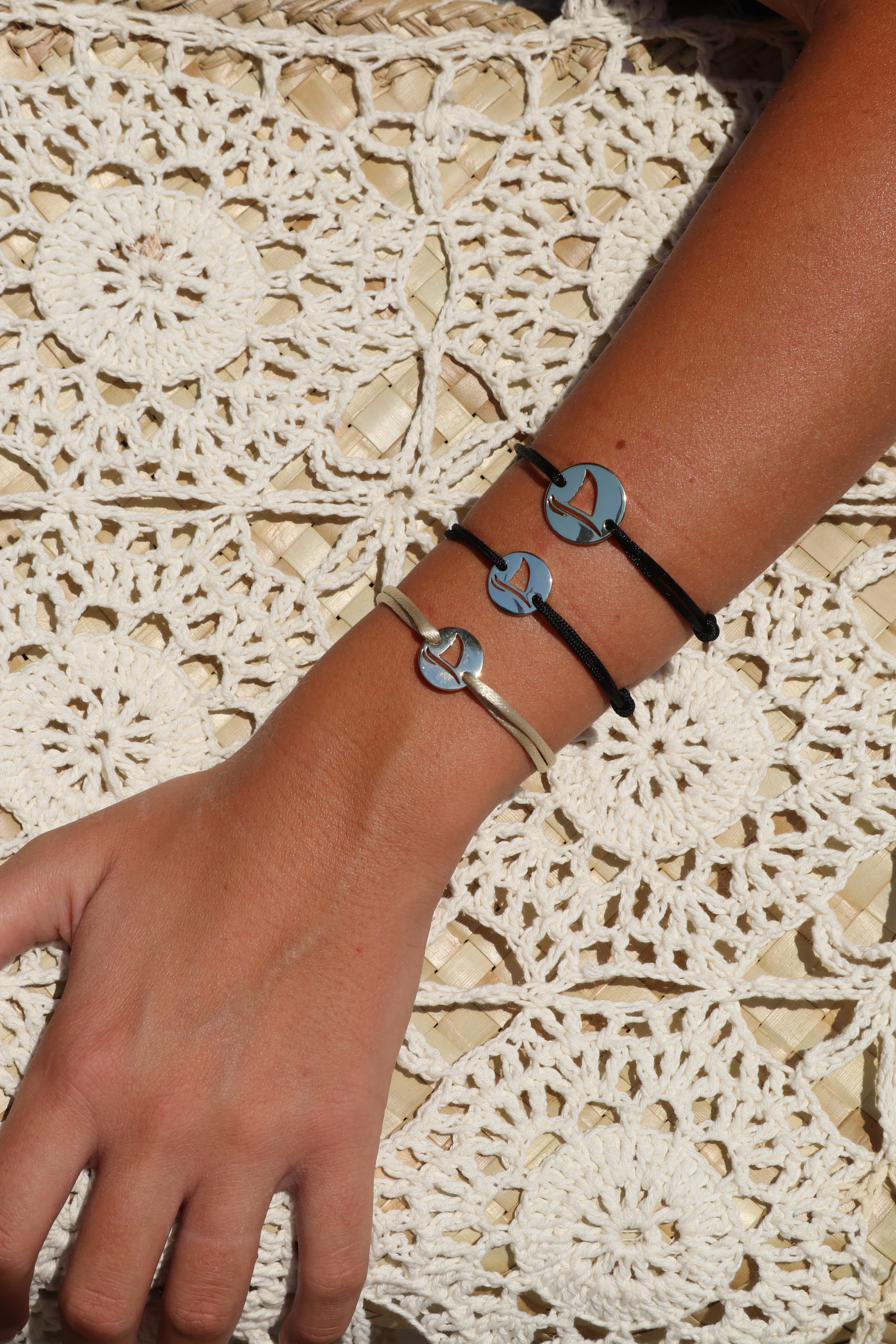 Three Gaab shark coin bracelets on a wrist resting on a woven cream mat